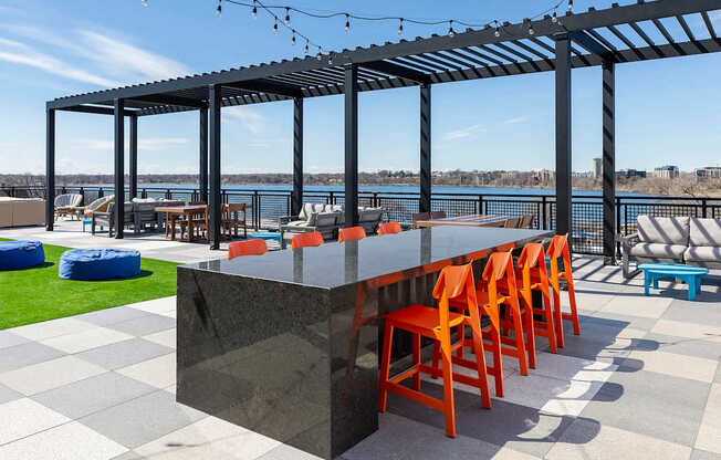 Bar with orange chairs and a black counter is set up on a patio with a view of the water.