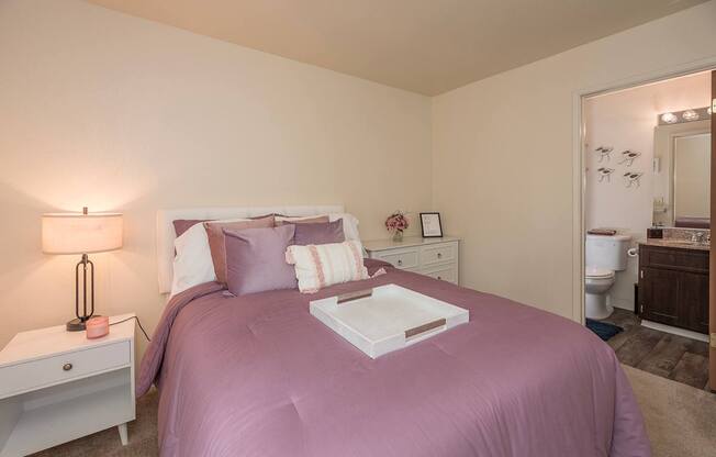 Model primary bedroom with a purple bedspread and a white nightstand with a lamp at Pheasant Pointe Apartments, California, 95833