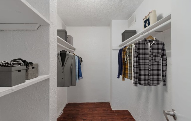 a walk in closet with clothes hanging on the wall