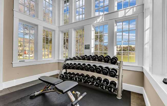 A home gym with a bench, weights, and windows.