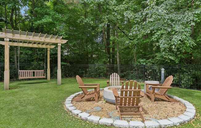 A wooden bench and chairs are arranged around a fire pit in a garden.