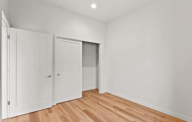 A room with white walls and wooden flooring with three white doors.