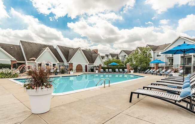 A pool surrounded by lounge chairs and umbrellas with a row of houses in the background