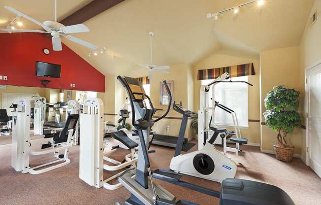 a gym with cardio machines and a ceiling fan