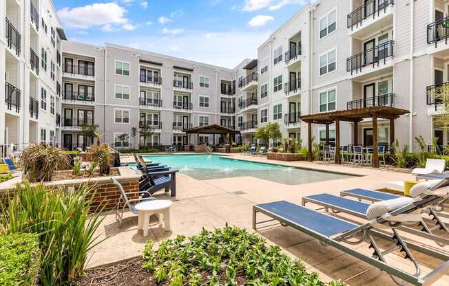 A pool area with sun loungers and a building in the background.