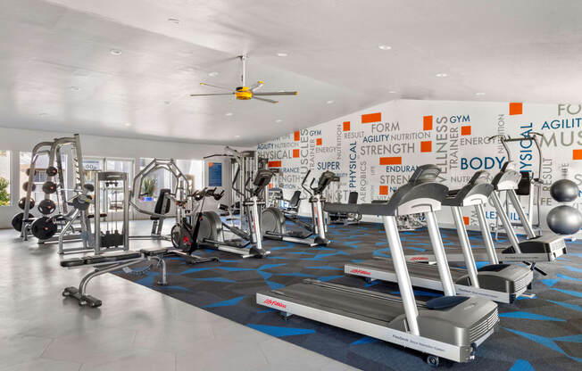 a large fitness room with cardio equipment and a ceiling fan