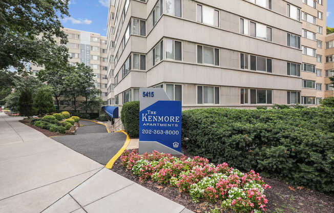 The entrance to The Kenmore Apartments with a blue sign and flowers in the foreground.