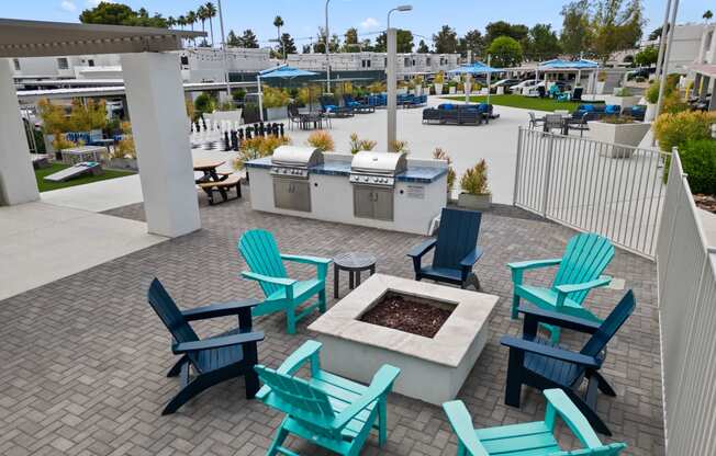 an outdoor patio with a firepit and turquoise adirondack chairs