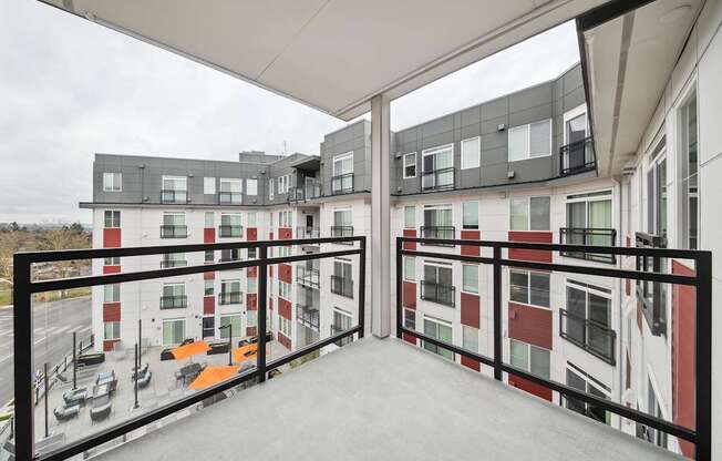 A balcony with a black railing and a view of a parking lot and buildings.