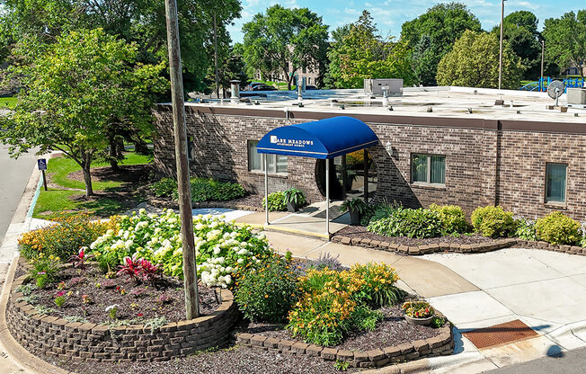 A flower bed in front of a brick building with a blue awning.