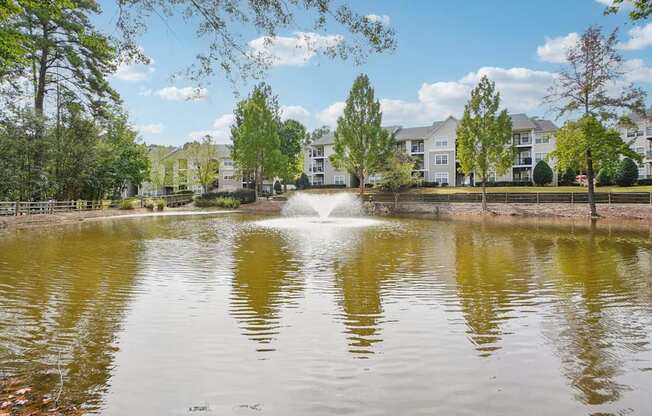 A fountain in the middle of a pond surrounded by trees and buildings.