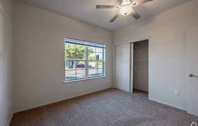 A room with a ceiling fan and a window overlooking a street.