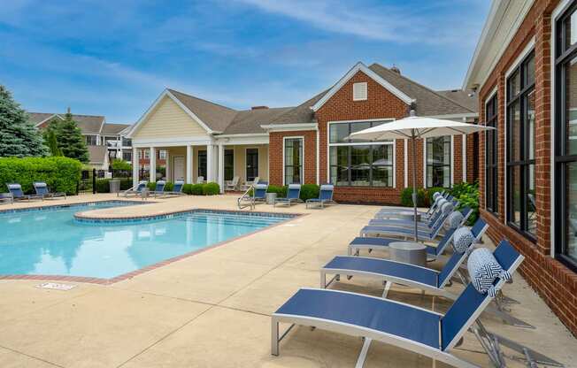 a swimming pool with chaise lounge chairs and umbrellas in front of a brick building