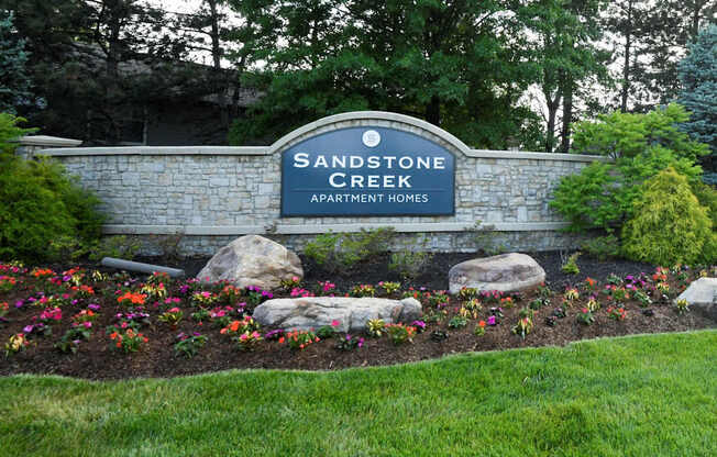 A sign for Sandstone Creek Apartment Homes is surrounded by flowers and rocks.