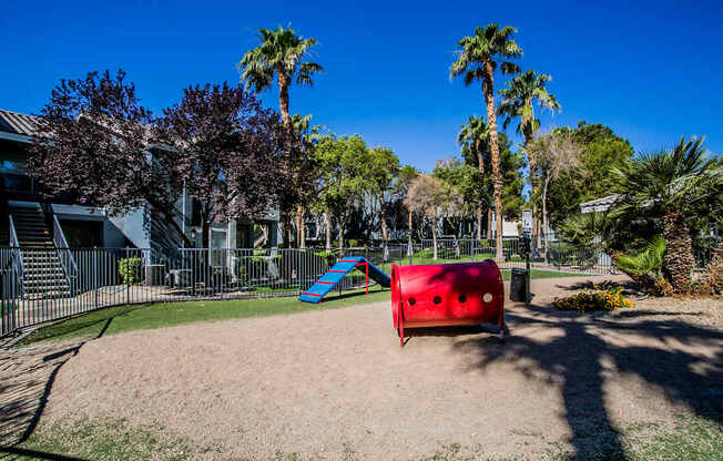 A playground with a red slide and a blue slide in the middle of a sandy area.
