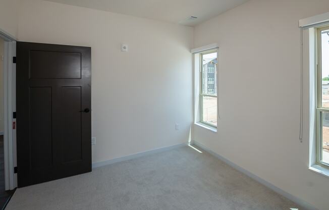 an empty living room with a black door and two windows at The Crossings at Windsong, Prescott Valley