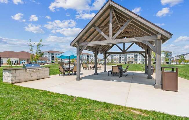 A pavilion with a roof and chairs is surrounded by a grassy area.