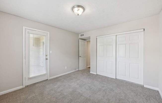 A bedroom with a carpeted floor, closet, and glass door leading to a balcony at Gwinnett Square Apartments in Duluth, GA