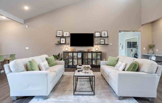 A modern living room with a white sofa set and a black television mounted on the wall.