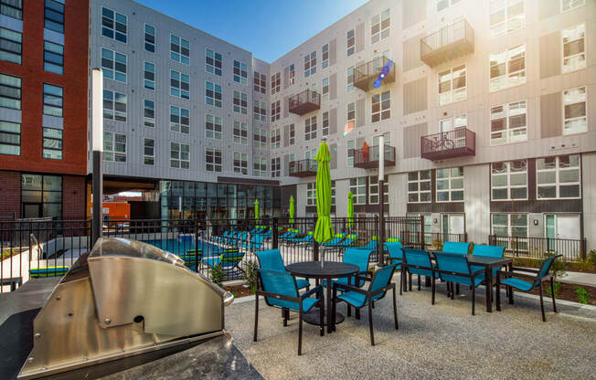 a patio with blue chairs and tables in front of an apartment building