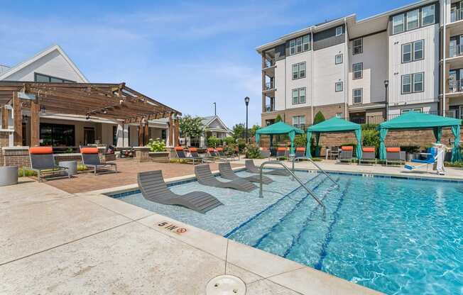 a swimming pool with lounge chairs and umbrellas next to an apartment building