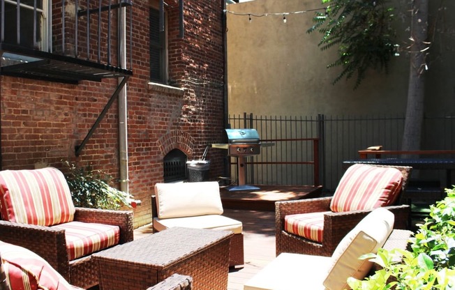 Brookmore Pasadena ca apartments back patio next to brick wall. Stained wood deck with cushioned wicker patio furniture and grill.