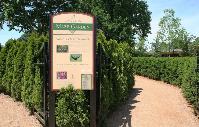 a sign for the maze garden in front of a row of hedges