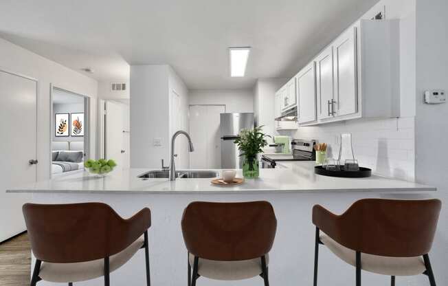 a kitchen with white cabinets and a counter with three chairs