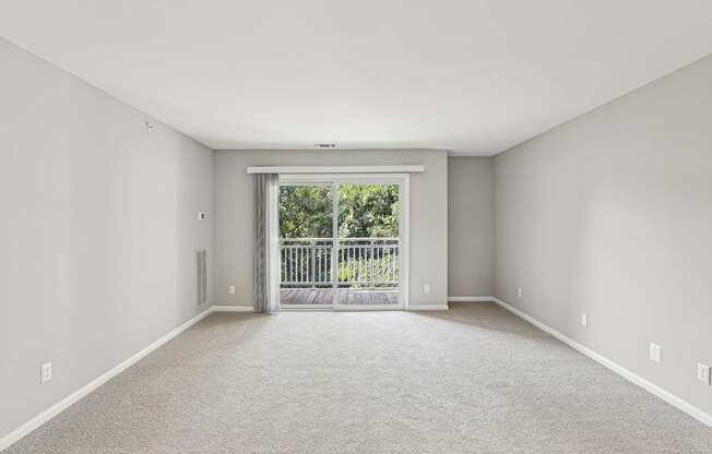 A spacious room with a carpeted floor and a sliding glass door leading to a balcony.