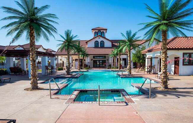 A resort-style swimming pool here at Andalucia Villas with clear blue water, a central spa, and palm trees lining the deck, surrounded by lounge seating and Spanish-style buildings that create a relaxing, upscale atmosphere.