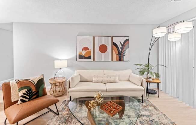 A living room with a white couch, a glass coffee table, and a chair.