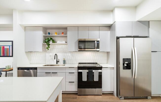 Light finish kitchen with soft gray cabinetry, quartz countertops, stainless steel appliances, matte black fixtures, and a tile backsplash.
