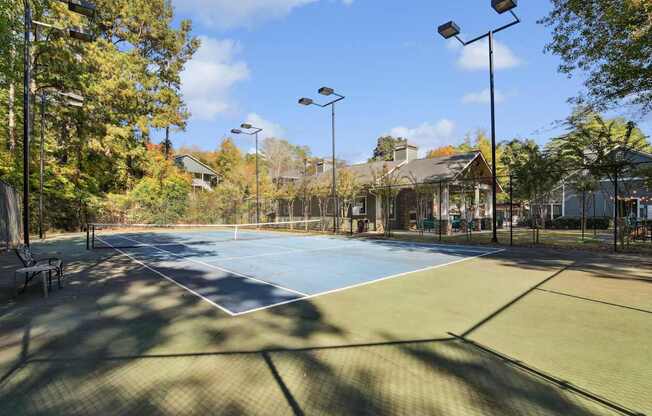 A tennis court surrounded by trees and street lights.