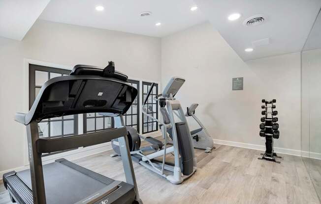 A treadmill, a stationary bike, and a set of dumbbells are in a well-lit room.