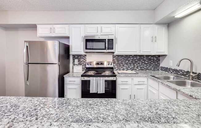 A kitchen with a refrigerator, microwave, oven, and sink.