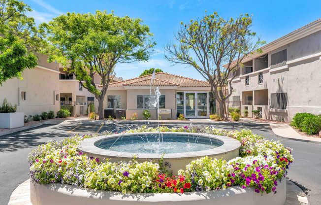 a fountain in front of an apartment building with flowers