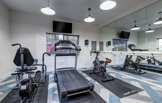 Two-Bedroom Apartments in Everett, Washington - Woodbrook - Fitness Center with Elliptical Machine, Treadmill, Stationary Bike, Mirror Wall, TV, and Window.