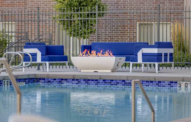 a fire pit in the middle of a pool with blue chairs around it