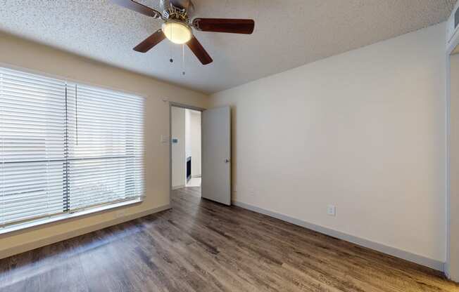 an empty living room with a large window and a ceiling fan