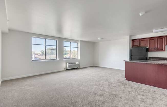 an empty living room with a kitchen and a window