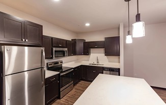 A modern kitchen here at The Park with dark espresso cabinets, stainless steel appliances, quartz counters, and a bright island, creating a sleek, spacious, and inviting cooking and gathering space.