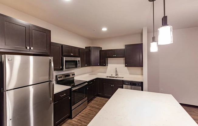 A modern kitchen here at The Park with dark espresso cabinets, stainless steel appliances, quartz counters, and a bright island, creating a sleek, spacious, and inviting cooking and gathering space.