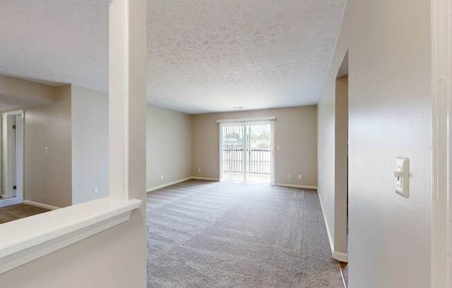 an empty living room and hallway with a door to a balcony