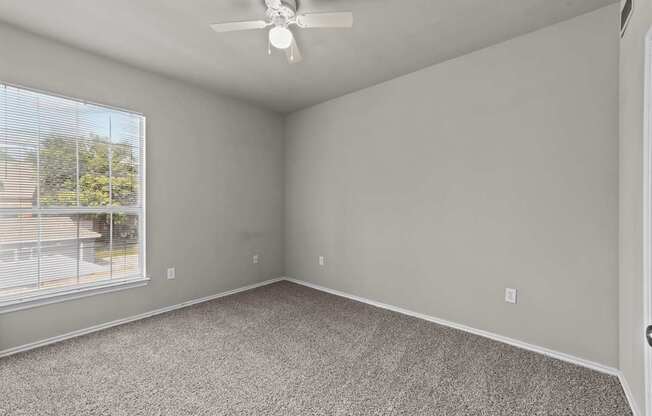 A room with a ceiling fan and a window overlooking a fence.
