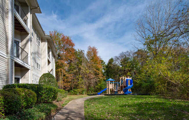 A playground with a blue slide is located in front of a white building.