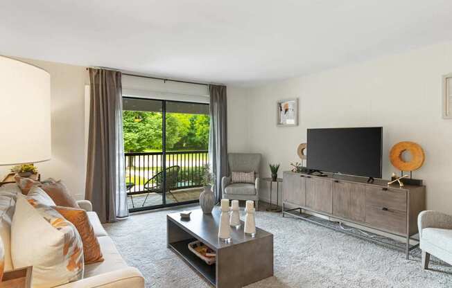 A living room with a white couch, a coffee table, a television, and a sliding glass door.