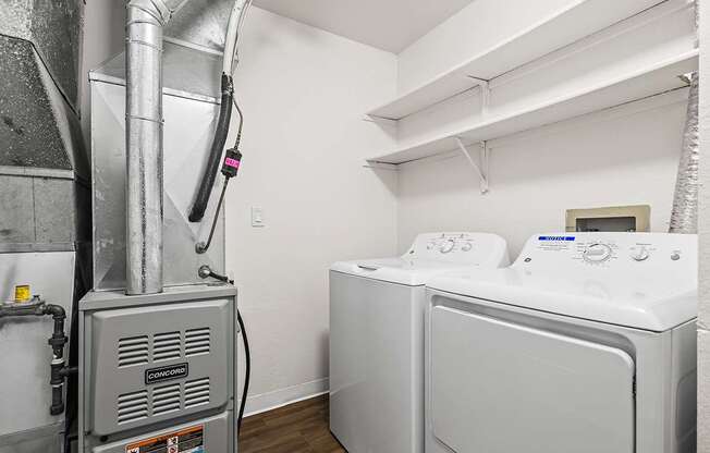 A washing machine is in a laundry room with a dryer and shelves at Tanglewood Apartments, Oak Creek, WI