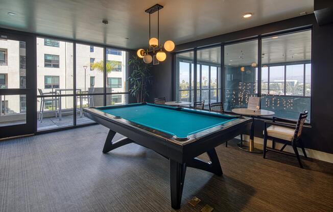 Game lounge with a pool table, bar seating, and large windows offering open views of the surrounding community.