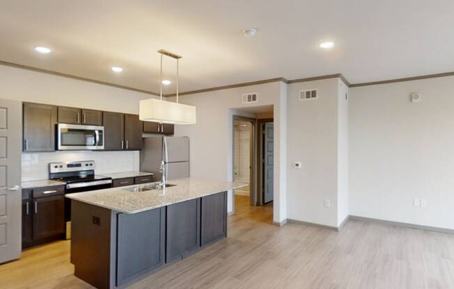 Modern kitchen here at 49 West Apartments view with a granite island, stainless steel appliances, and dark cabinetry. Bright lights create a welcoming, spacious atmosphere.