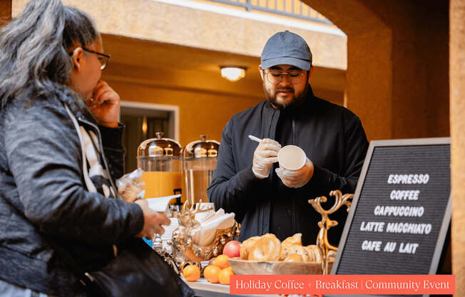 A man in a black outfit is serving coffee to a customer at a holiday coffee breakfast community event.